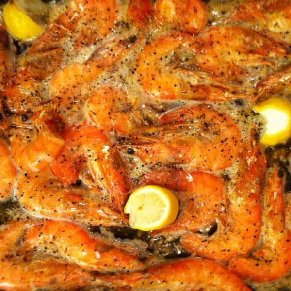 Shrimp in a baking dish with lemon wedges.