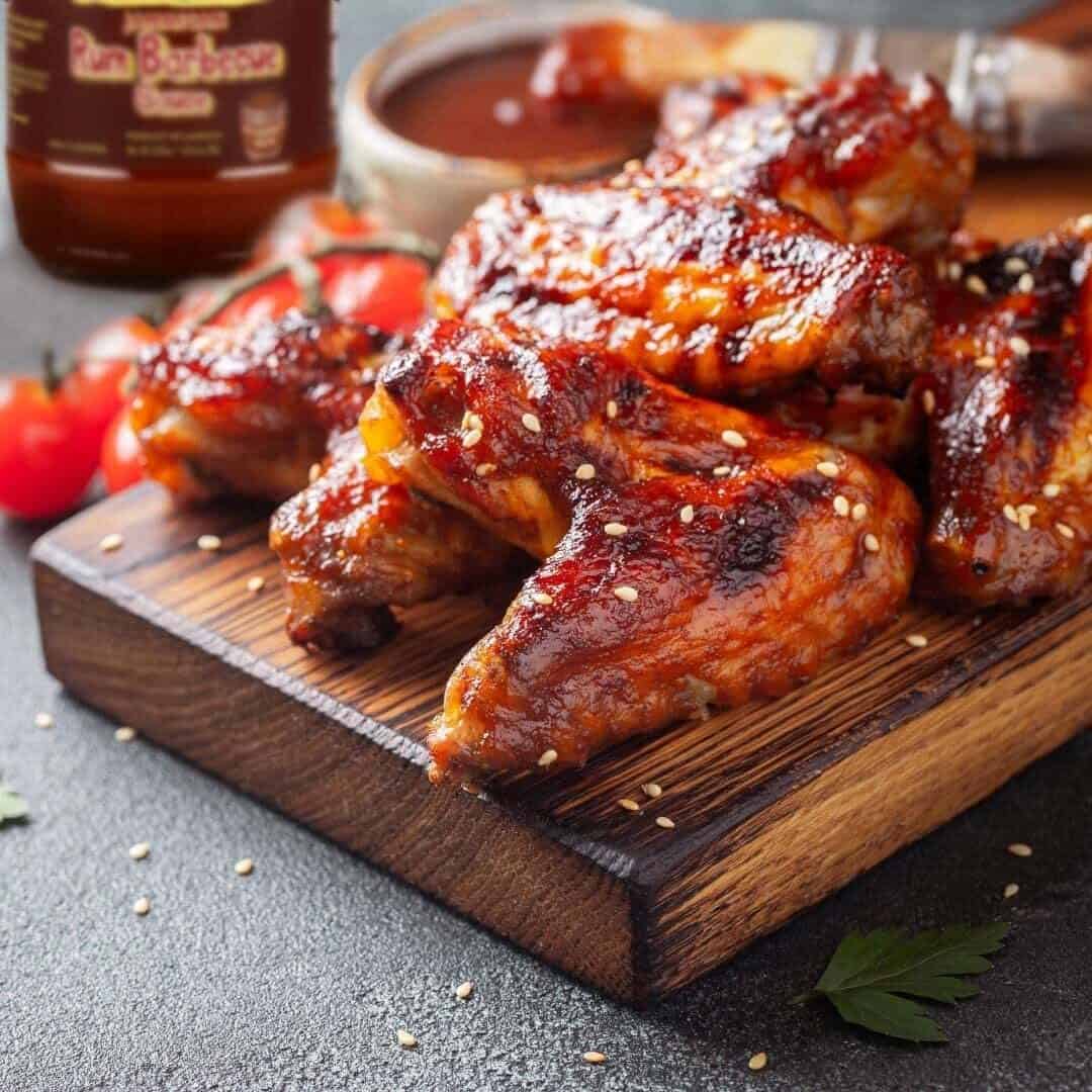 Bbq chicken wings on a wooden cutting board with a bottle of bbq sauce.