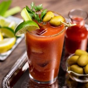 A bloody mary with lime and olives on a tray.